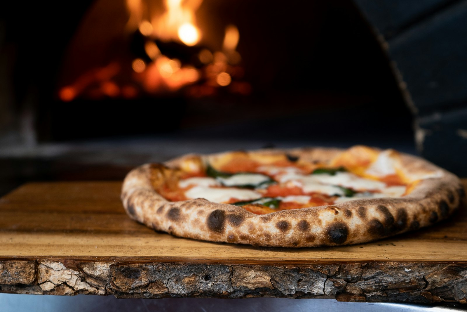 Pizza recién horneada frente al horno de leña encendido